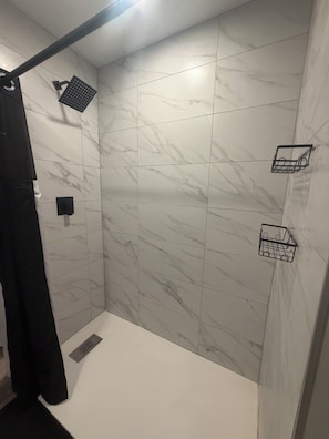Un espacio de ducha con pared de mármol blanco, una toalla negra y un pequeño estante negro.