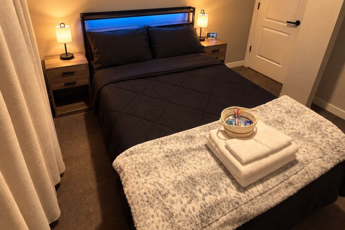Habitación de hotel con cama, lámparas de noche, mesita de noche, una puerta y una ventana con persianas.