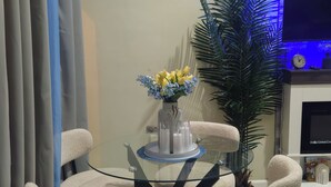 Un comedor con una mesa de vidrio rodeada por cuatro sillas, un jarrón con flores amarillas y una planta en maceta.