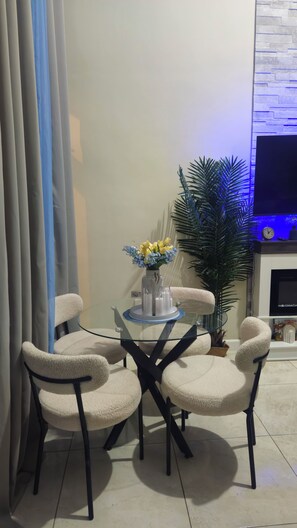 Un comedor con una mesa de vidrio rodeada por cuatro sillas, un jarrón con flores amarillas y una planta en maceta.