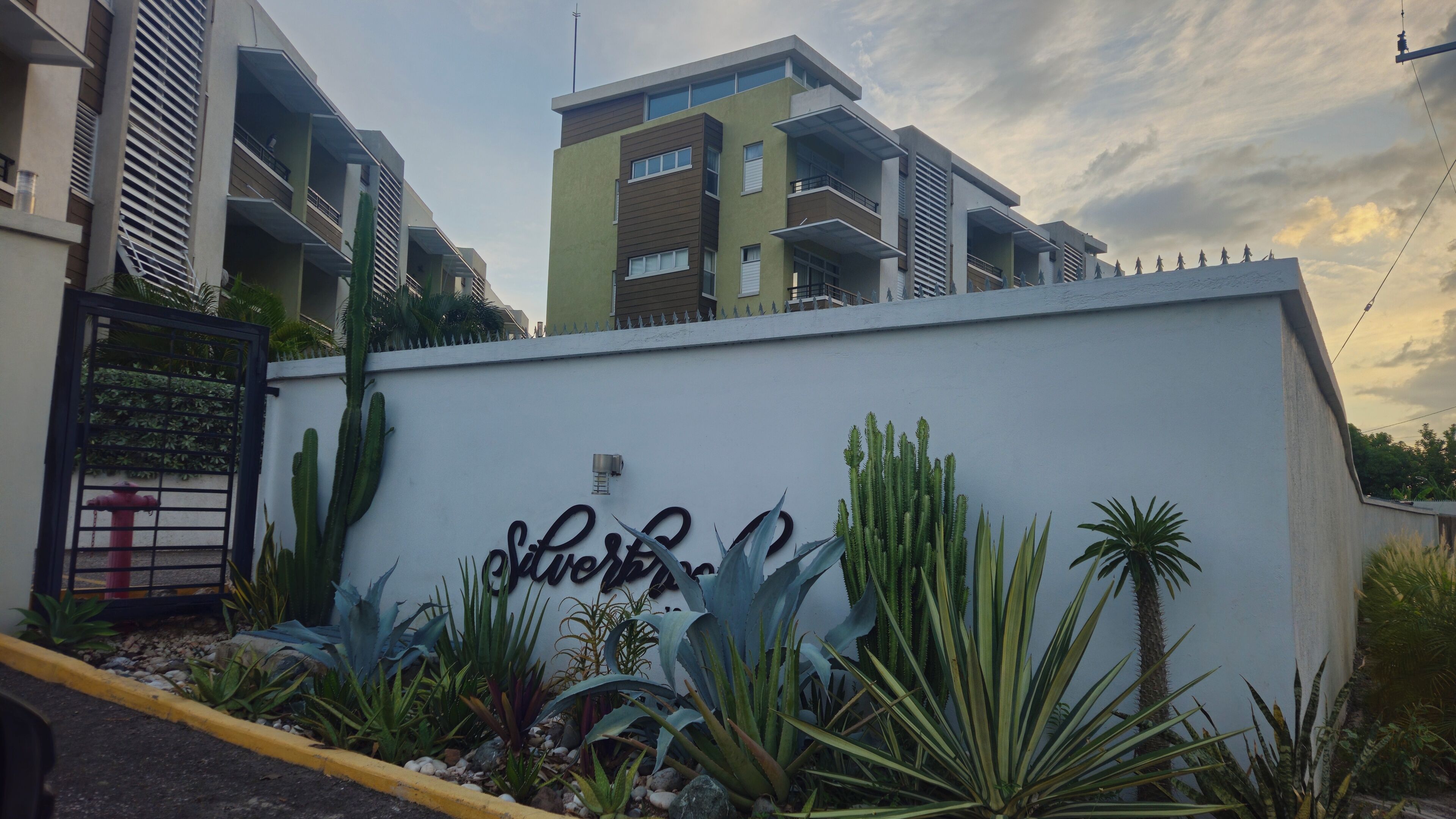 A modern building with a flat roof, a gated entrance, and a wall with a sign.