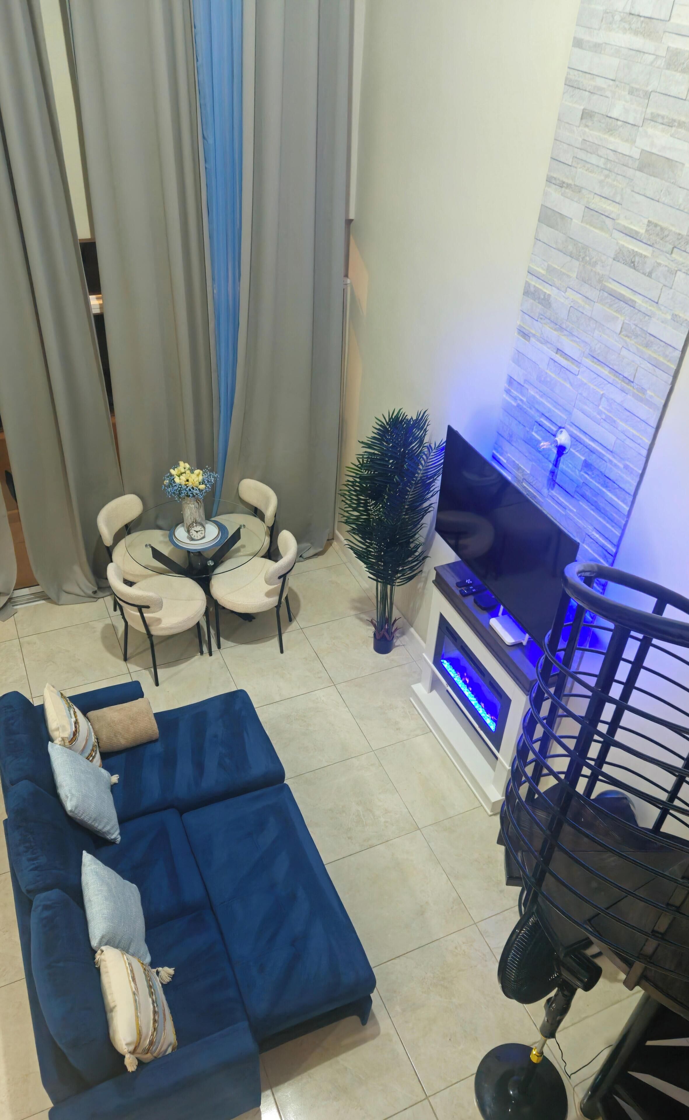 A living room with a blue sofa, a small round table with chairs, a TV, and a decorative plant.