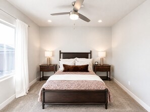 Ein Schlafzimmer mit einem Bett, zwei Nachttischen, einem Deckenventilator und einem Fenster mit Vorhängen.