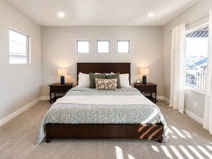A bedroom with a large bed, two bedside tables, a headboard, and a window with curtains. - Desert Light Retreat | Lazy River & Splash Pad! (Hurricane)