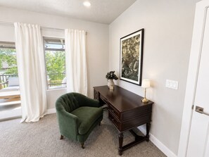 A room with a green armchair, a dark wooden desk, a framed picture on the wall, and a window with white curtains. - Desert Light Retreat | Lazy River & Splash Pad! (Hurricane)