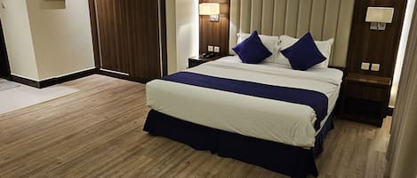 Et hotelværelse med en stor seng, trægulv, lukket dør og et maleri på væggen.