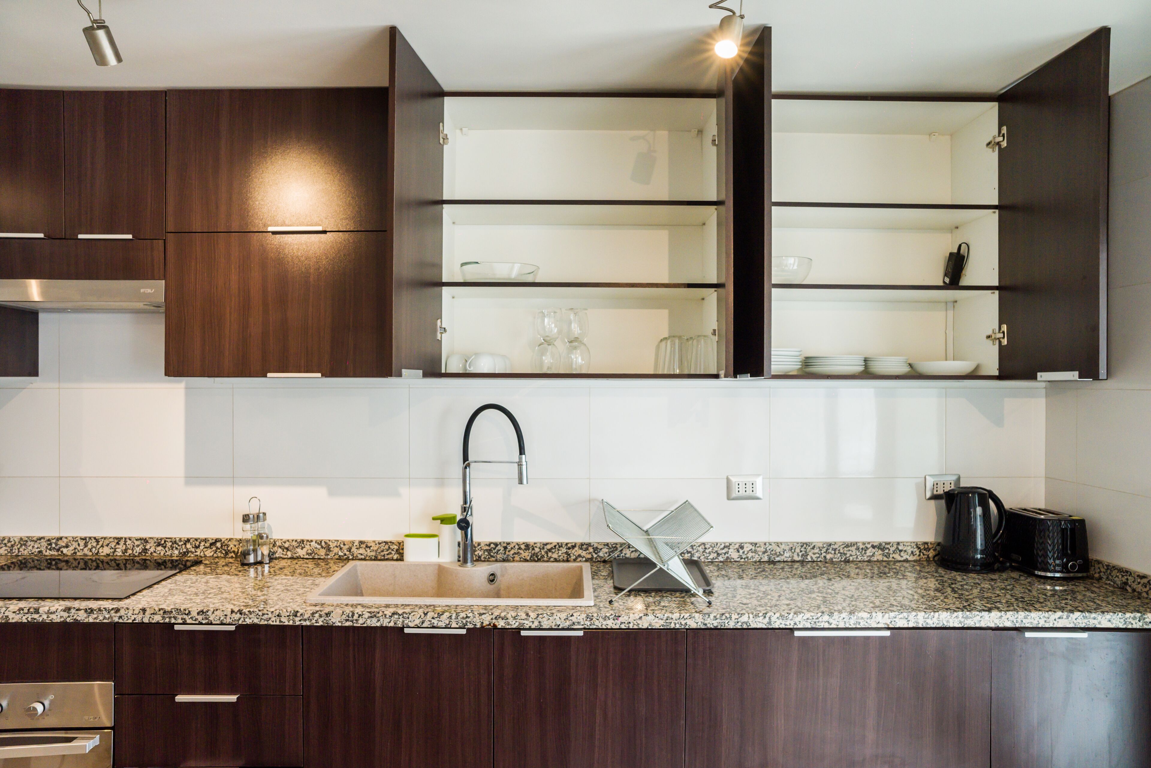 A modern kitchen with dark wood cabinets, a granite countertop, a stainless steel sink, and a built-in wine rack.