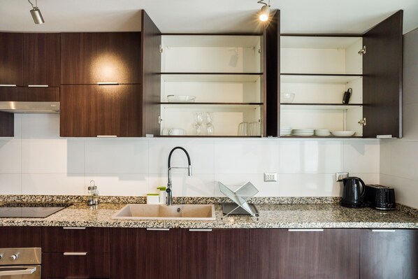 A modern kitchen with dark wood cabinets, a granite countertop, a stainless steel sink, and a built-in wine rack.