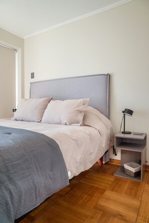 A bedroom with a bed, a nightstand, a lamp, and a storage box.