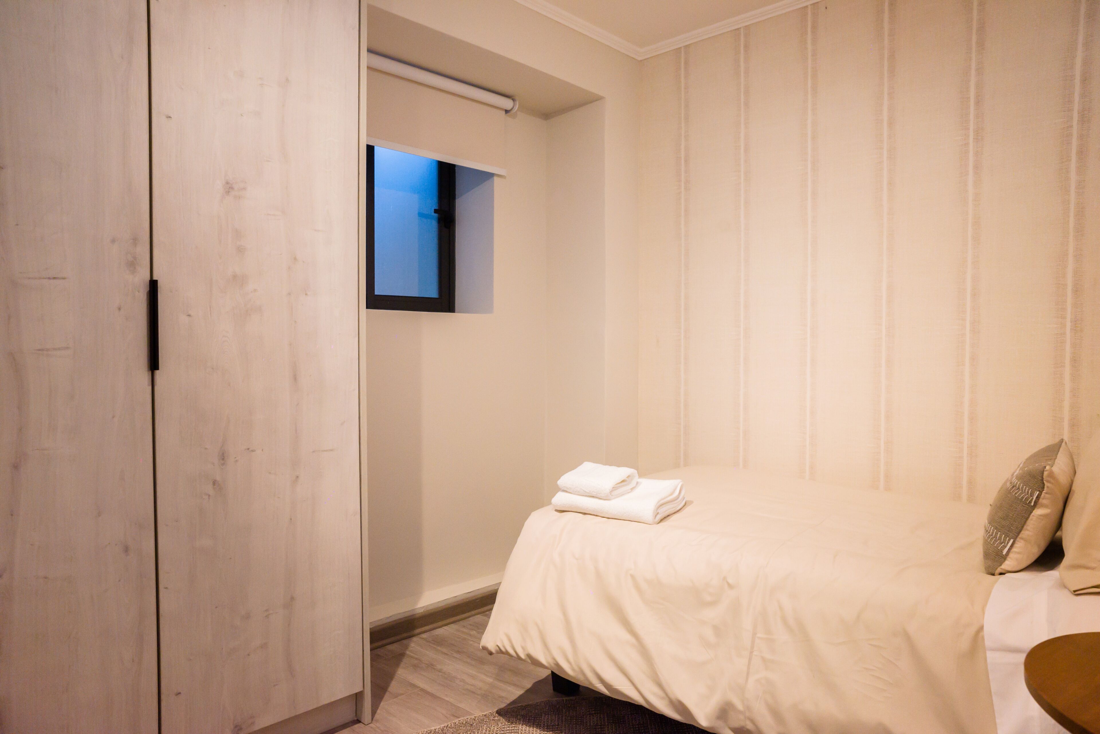 Una habitación de hotel con una cama, un ventanal pequeño y un armario.
