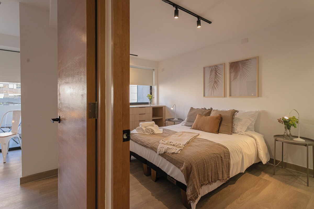A bedroom with a bed, bedside tables, a desk, and a window.