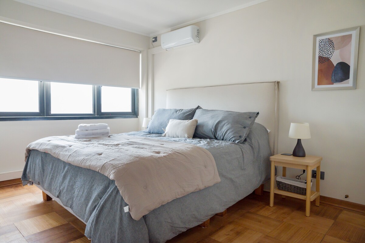 A bedroom with a bed, bedside table, lamp, and artwork on the wall.