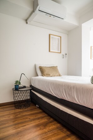 A bedroom with a bed, a bedside table with a plant, a framed picture on the wall, and an air conditioning unit above the bed. - Vitacura Apartments by Andes STR (Las Condes)