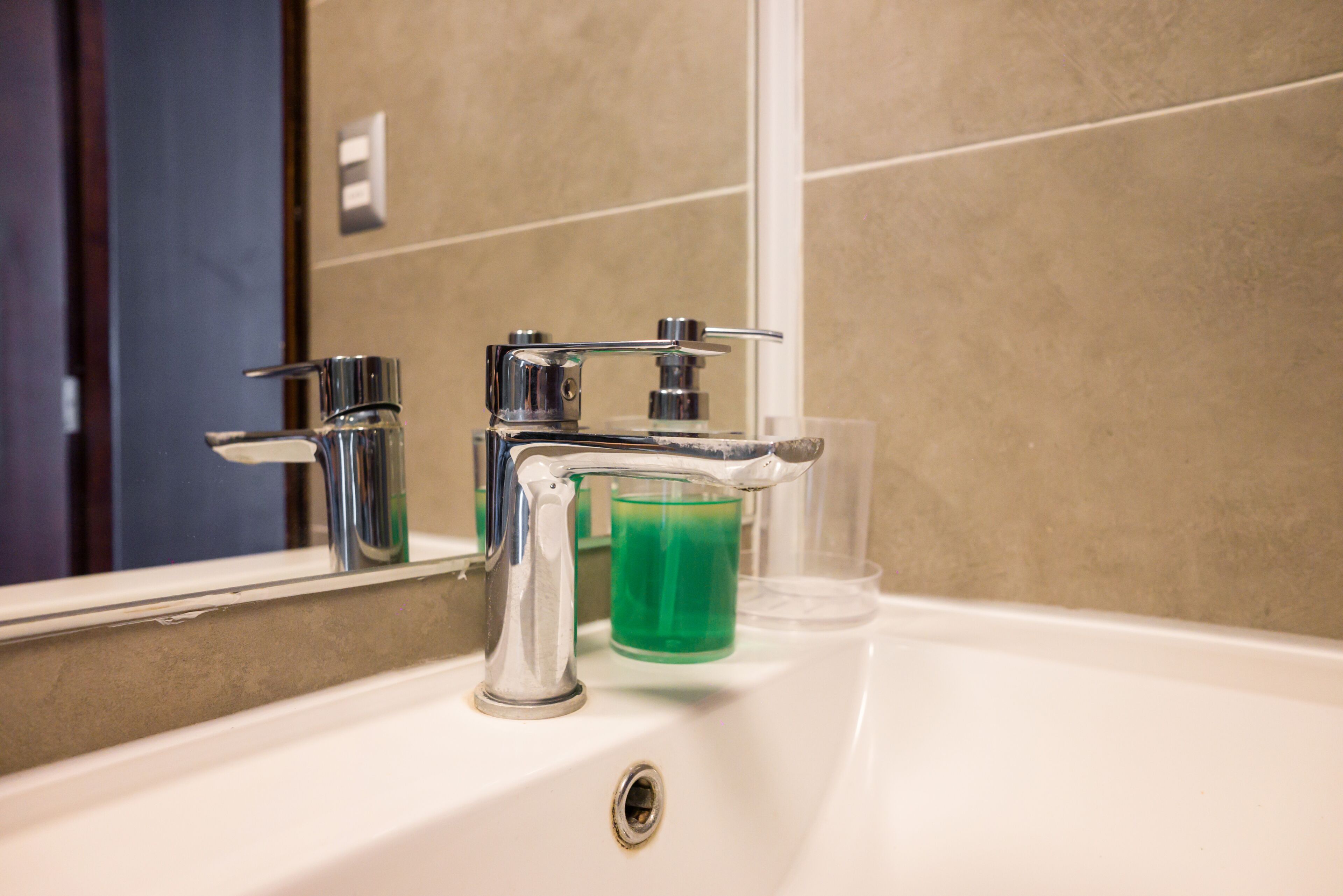 A bathroom sink with a chrome faucet and a glass of green liquid.