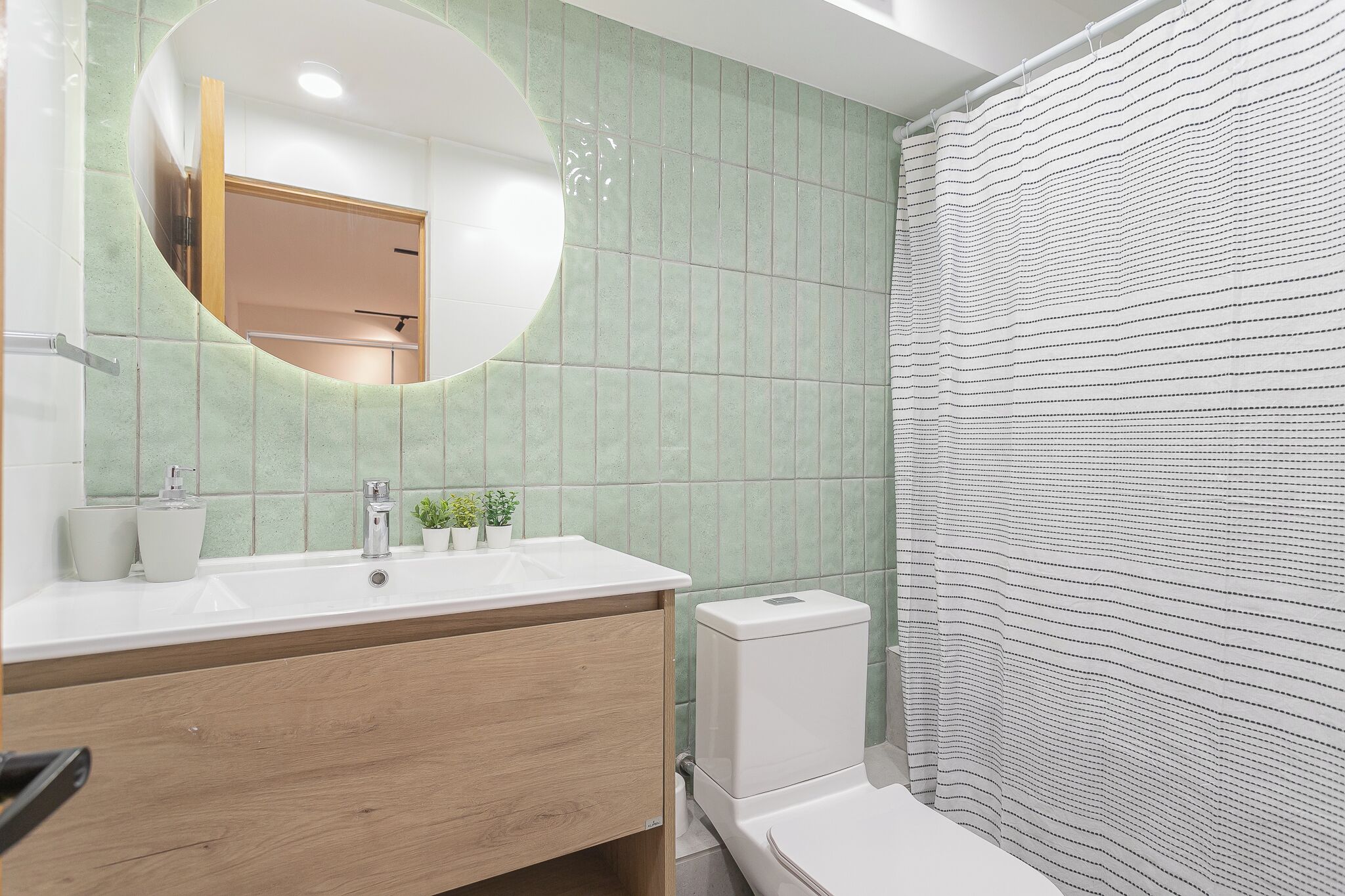 A bathroom with a round mirror, a sink, a toilet, and a shower curtain.
