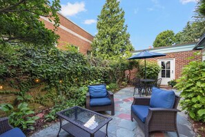 A patio area with wicker furniture, a glass table, and a brick building in the background. - The Secret Garden at Benefit~

Tranquil, starlit views in PVD with Parking! (Providence)