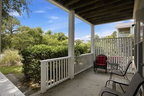 Ein überdachter Balkon mit weißer Reling, ein Korbstuhl mit rotem Sitzkissen und ein Tisch.