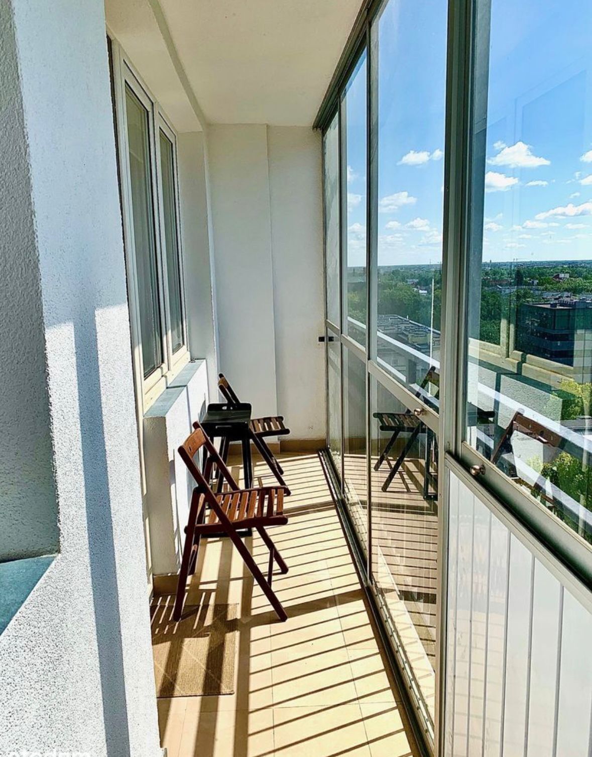 Een balkon met uitzicht op een stadsgezicht, voorzien van een houten vloer en twee houten stoelen.