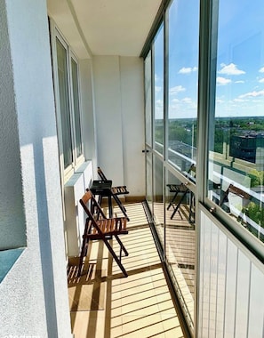Ein Balkon mit Blick auf eine Stadtlandschaft, mit Holzboden und zwei Holzstühlen.