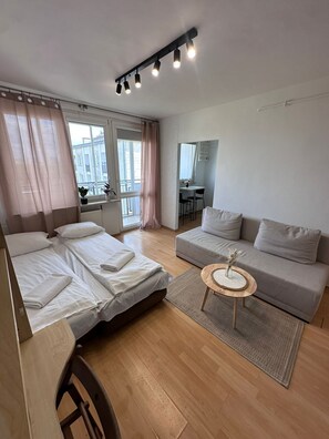 A modern hotel room with a bed, a sofa, a small round table, and a view of the city through the window.