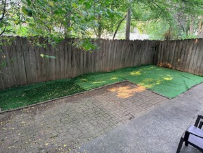 A backyard with a wooden fence, green artificial turf, and a brick patio area. - Charming 3-bedroom townhome with AC in Coeur D’Alene (Coeur D’Alene)