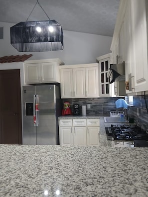A kitchen with white cabinets, a stainless steel refrigerator, a gas stove, and a hanging light fixture.