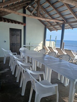 An outdoor seating area with a long table and chairs, a wooden door, and a view of the sea. - Boni Beach (Sonsonate)