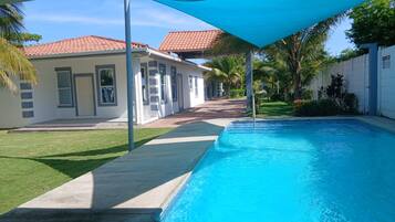 A swimming pool with a clear blue water surface, surrounded by a concrete deck and a blue shade sail.