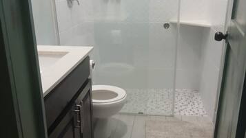 Une salle de bain comprenant des toilettes, un espace douche et un meuble-lavabo avec un miroir.