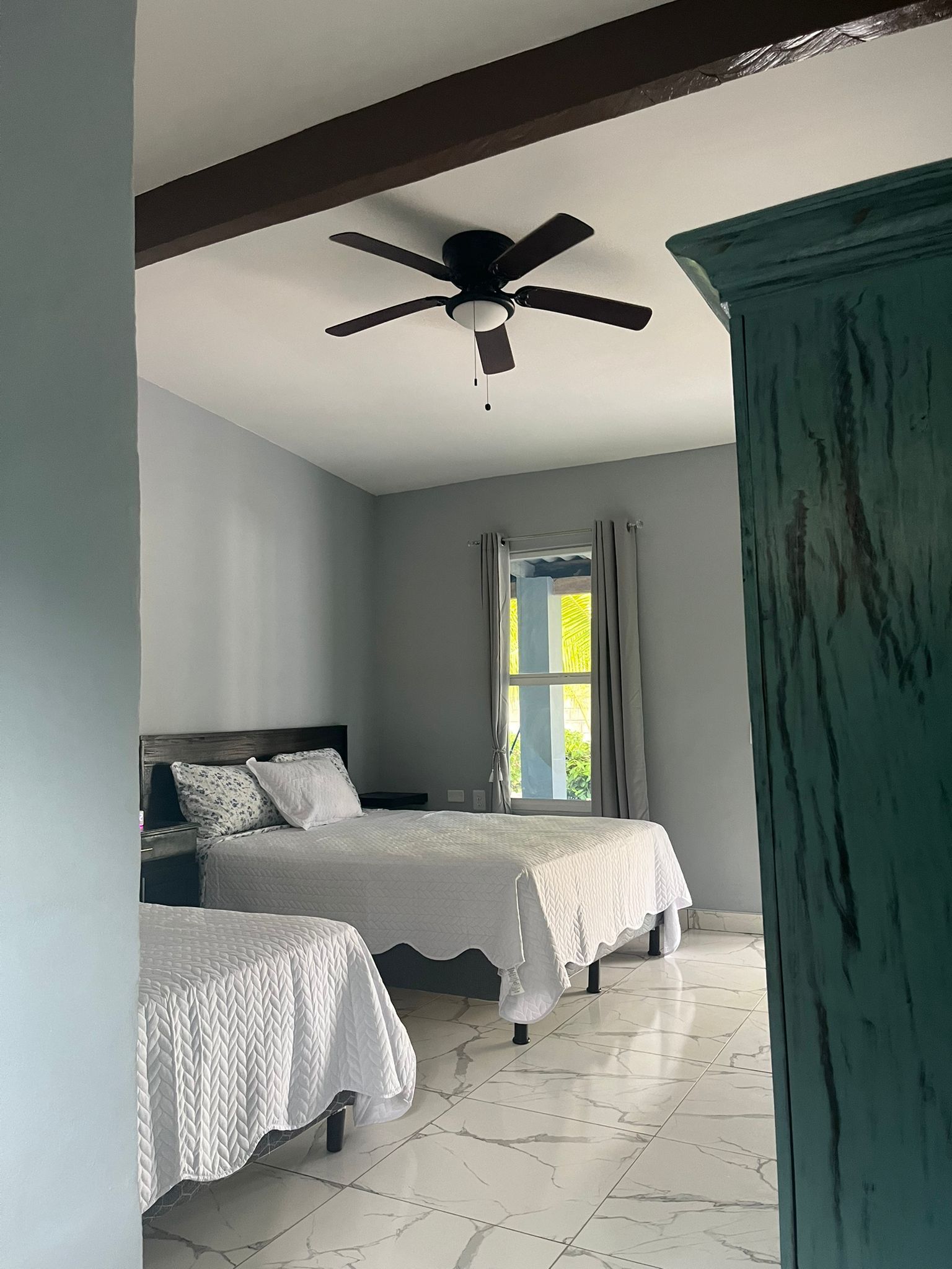 Un dormitorio con dos camas, un ventilador de techo, una ventana con cortinas y un armario color turquesa.