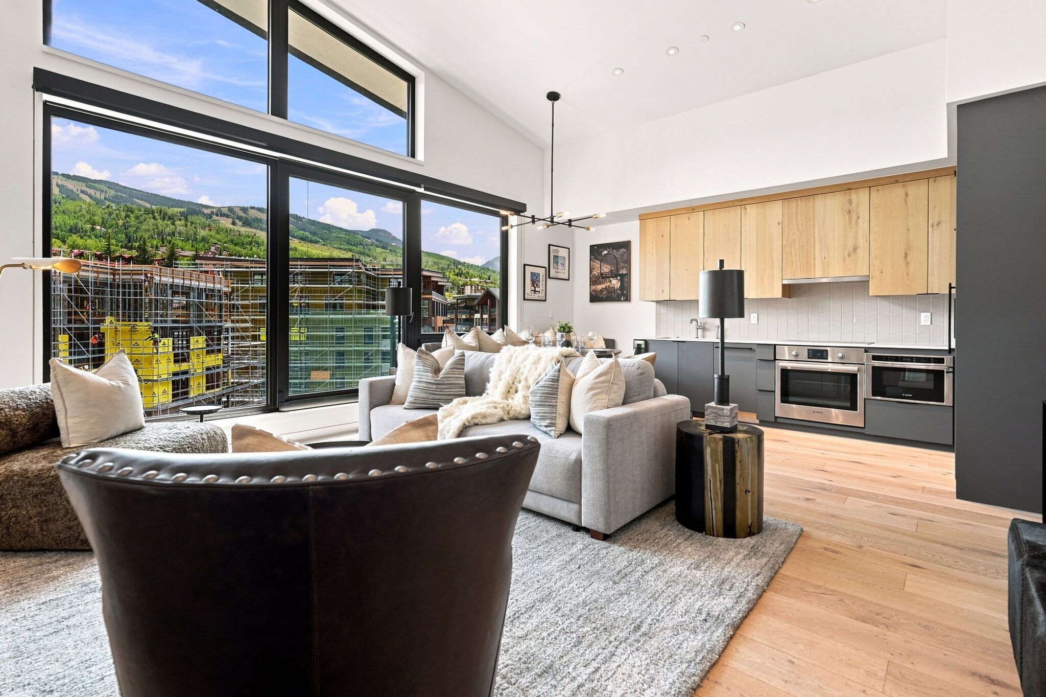 Una sala de estar moderna con un sofá, una mesa de centro y vistas a una obra en construcción a través de amplios ventanales.