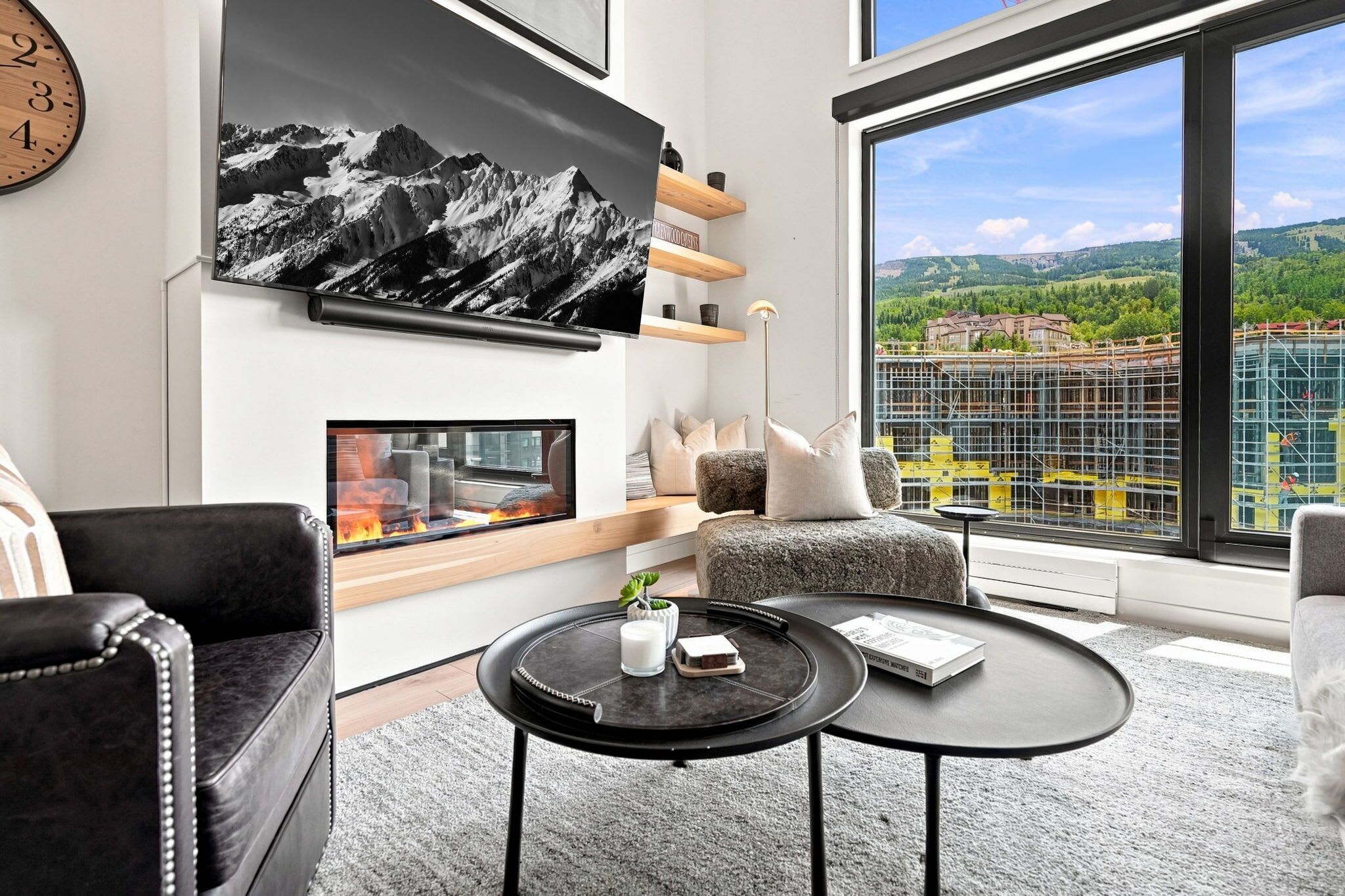 Ein modernes Wohnzimmer mit Kamin, einem großen Fenster mit Blick auf eine Baustelle und einer gemütlichen Sitzecke.