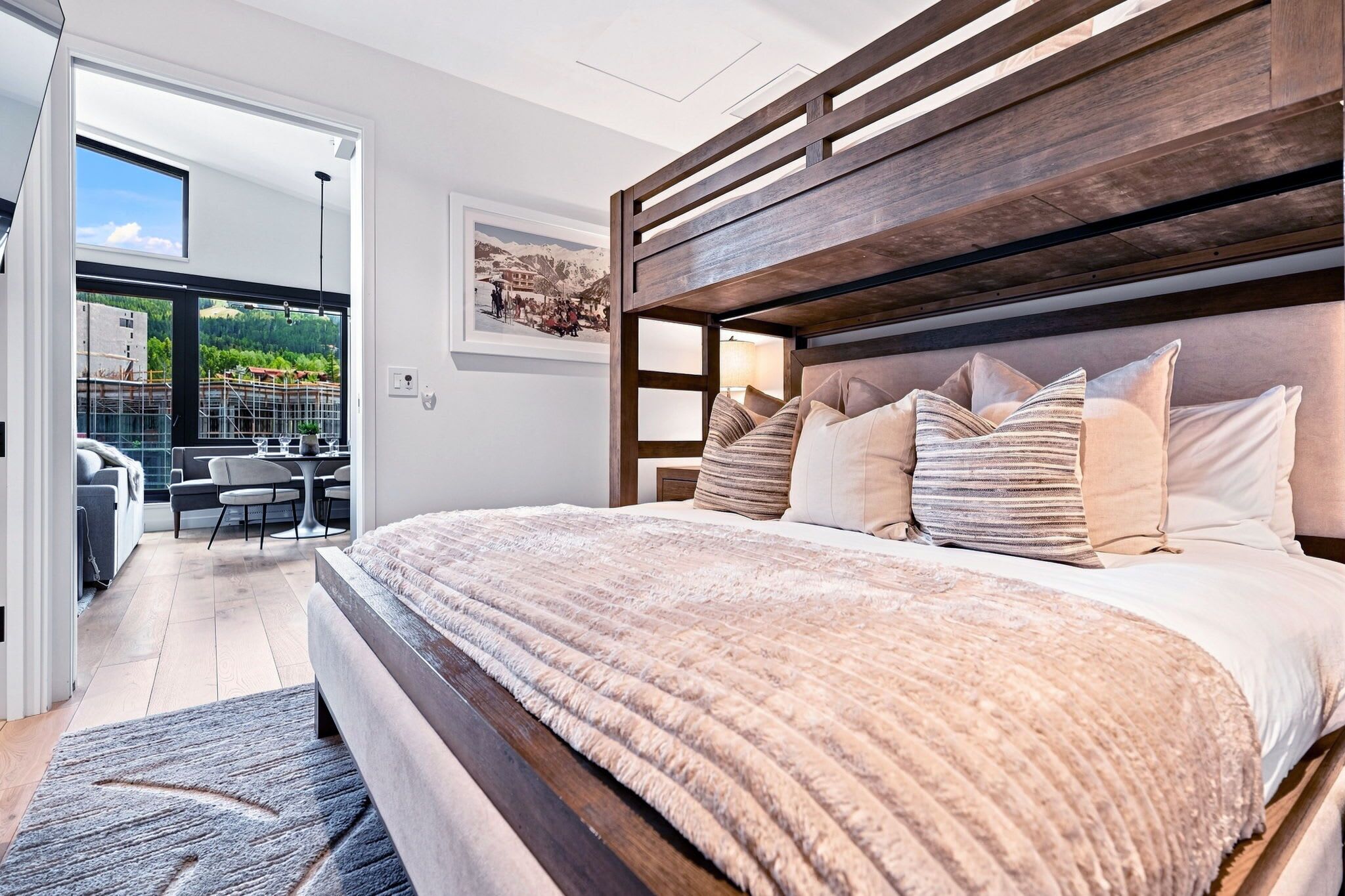 A modern bedroom with a large bed, wooden headboard, and a view of a balcony with outdoor furniture.