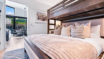 A modern bedroom with a large bed, wooden headboard, and a view of a balcony with outdoor furniture.