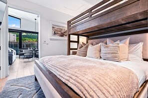 Ein modernes Schlafzimmer mit einem großen Bett, einem Holzkopfteil und Blick auf einen Balkon mit Gartenmöbeln.