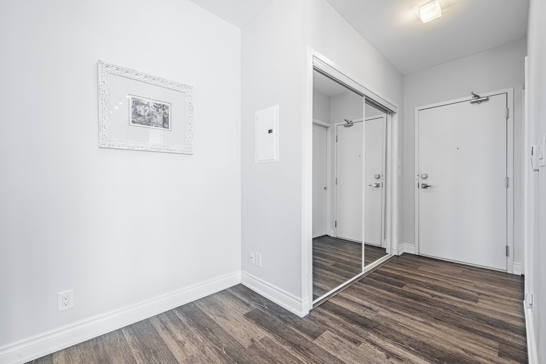 A hallway with a wooden floor, a white door, and a mirror on the wall.
