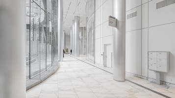 A corridor with glass walls, white marble flooring, and a sign indicating a location.