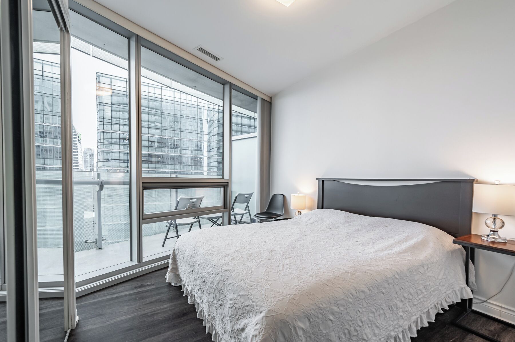 A hotel room with a large window, a bed, a desk with a lamp, and a chair.