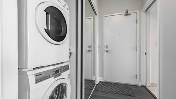 A laundry room with stacked washers and dryers, a door, and a doormat.