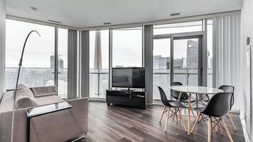 A modern living room with a sofa, a TV, and a dining area with chairs and a table.