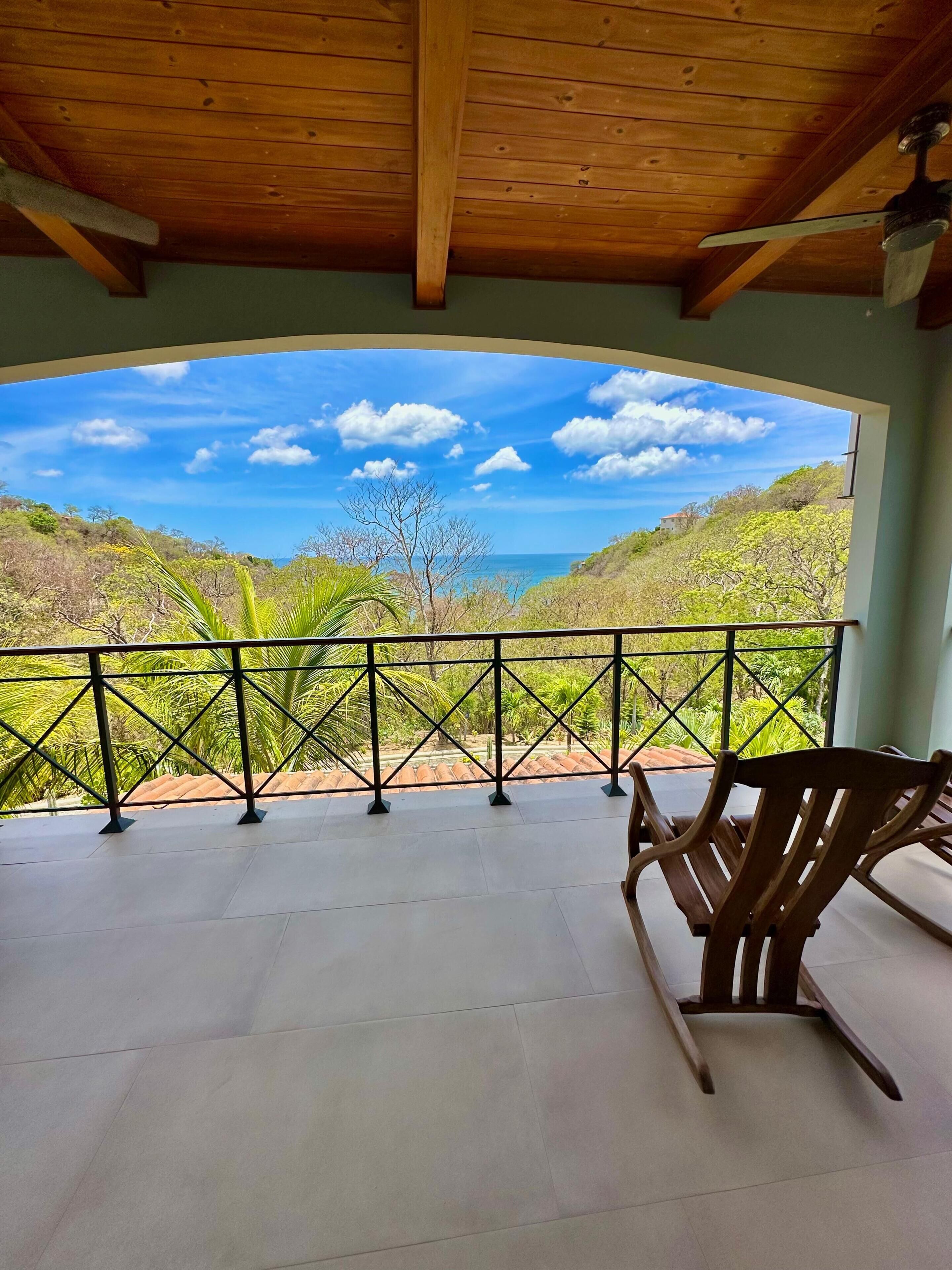 A covered outdoor area with a view of a hilly landscape and the sea.