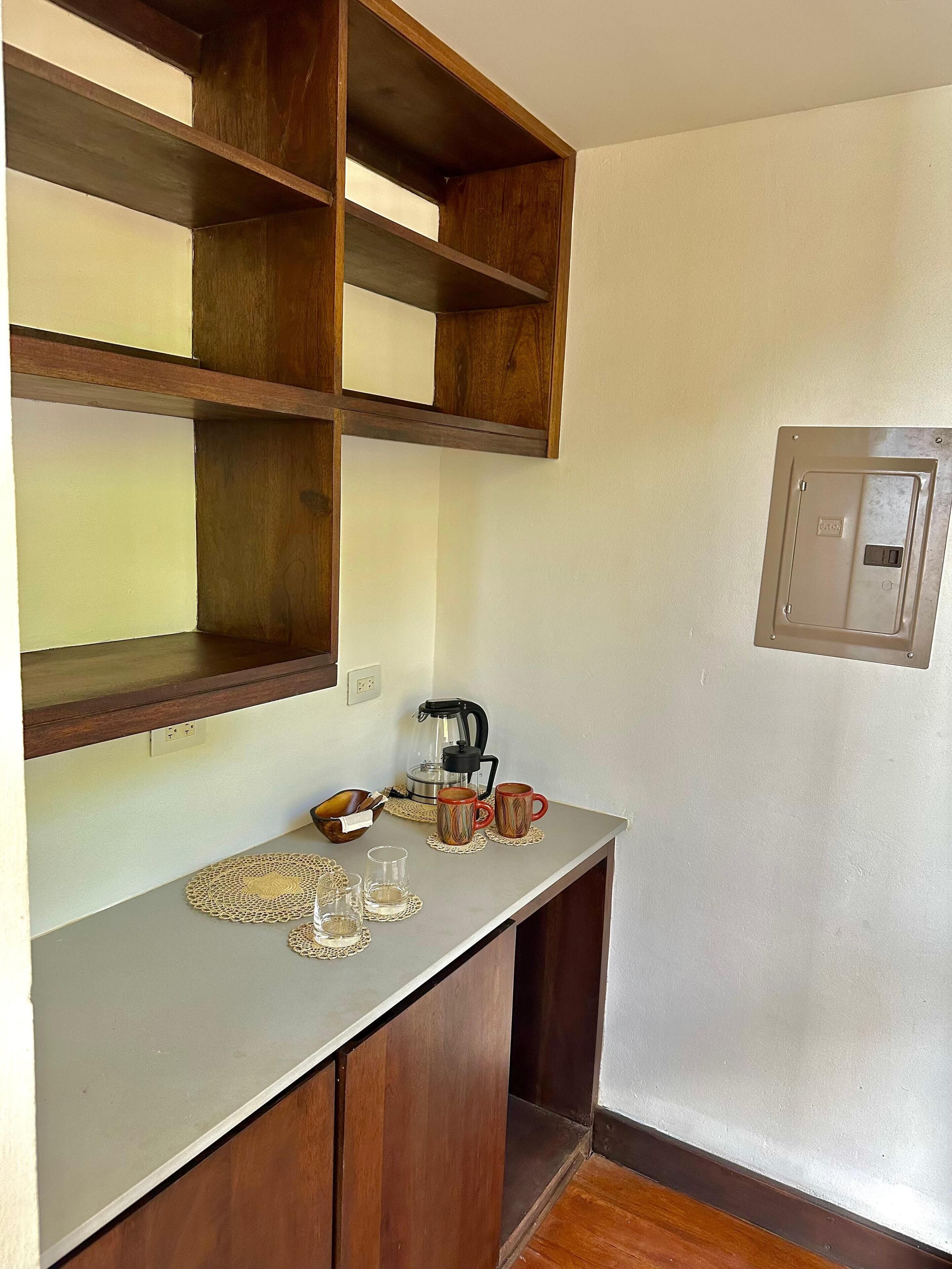 Una kitchenette con armarios de madera, una cafetera y dos tazas sobre una encimera.