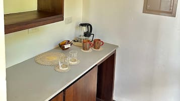 Una kitchenette con armarios de madera, una cafetera y dos tazas sobre una encimera.