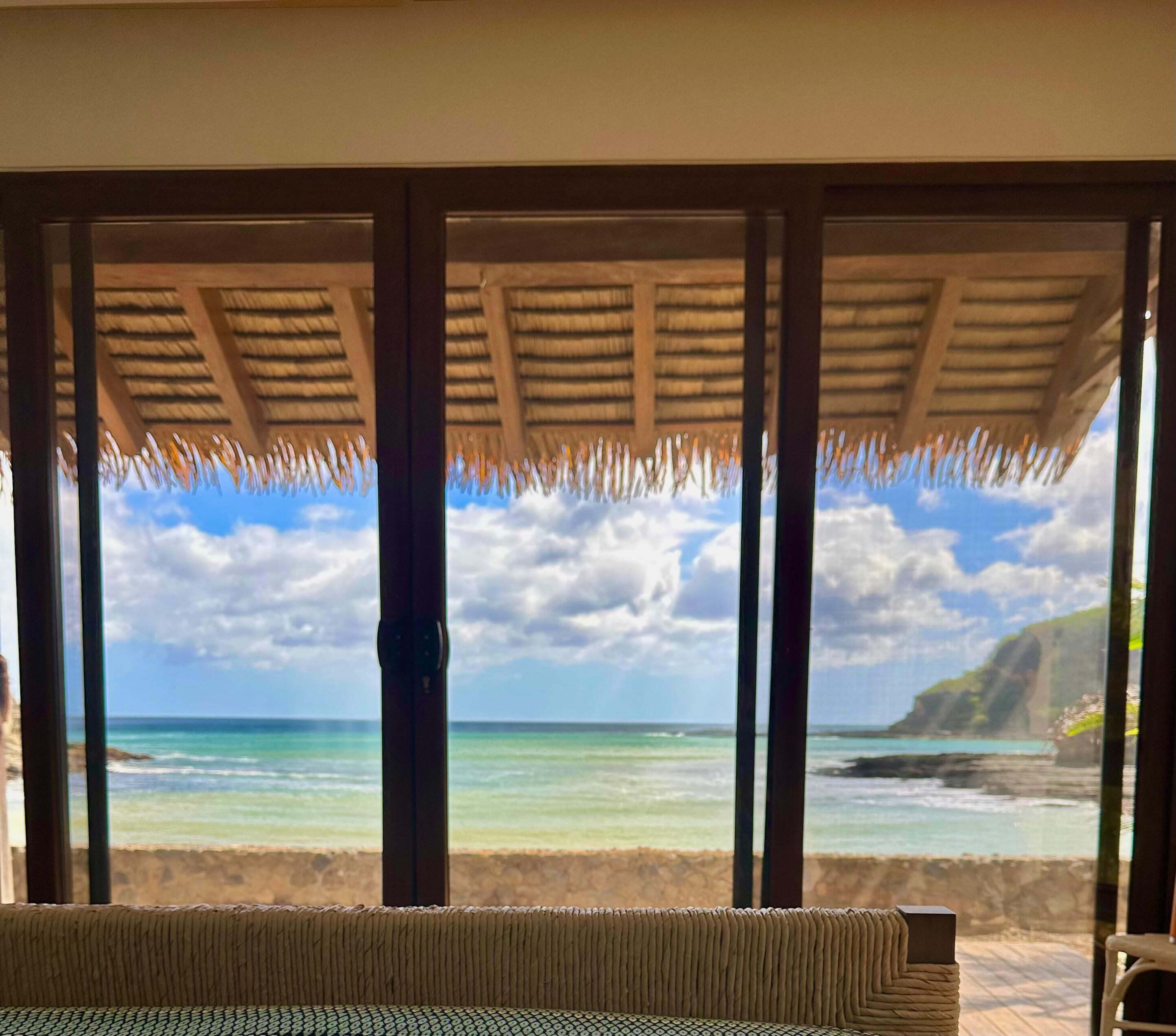 Um quarto com vista para o oceano, um telhado de palha e um sofá estampado.
