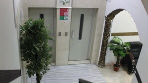 Un couloir avec un pot de plante, une porte avec une pancarte et un escalier muni d’une rampe.
