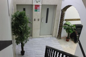 Un pasillo con una planta en maceta, una puerta con un letrero y una escalera con barandilla.