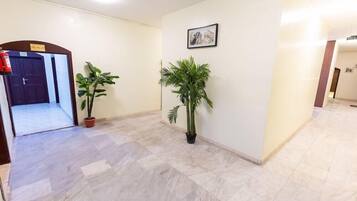 A hallway with a tiled floor, a potted plant, and a framed picture on the wall.
