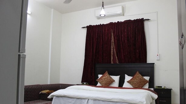 A bedroom with a bed, a nightstand, a wall-mounted air conditioner, and a window with a curtain.