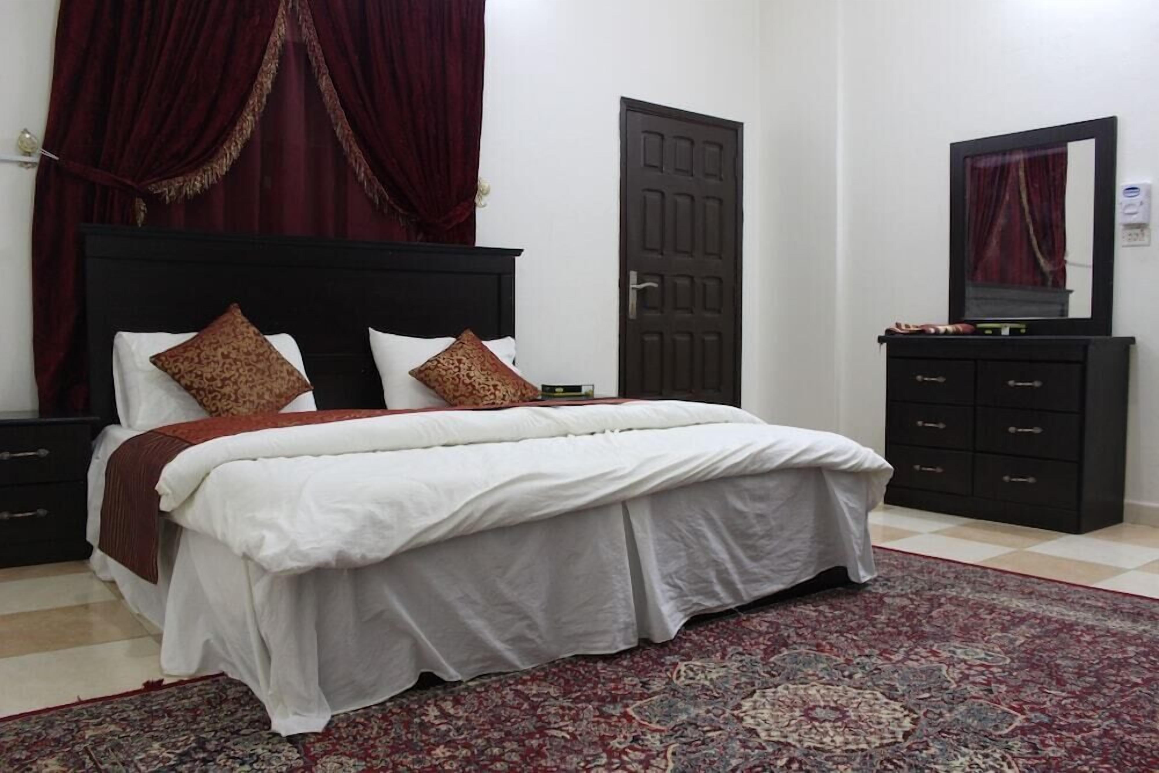 A bedroom with a bed, a nightstand, a dresser, a door, and a mirror.
