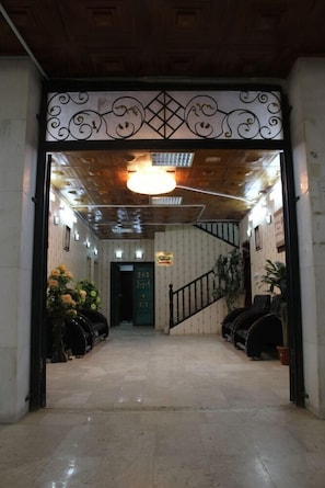 A hotel lobby with a wooden ceiling, a staircase, and potted plants.